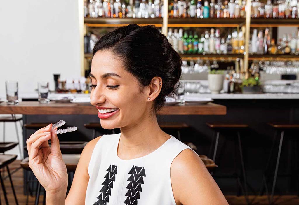 Woman holding a clear Invisalign aligner in a restaurant