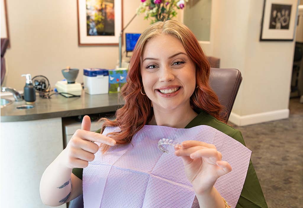 Woman holding a clear Invisalign aligner at a Kelleher Orthodontics Office.